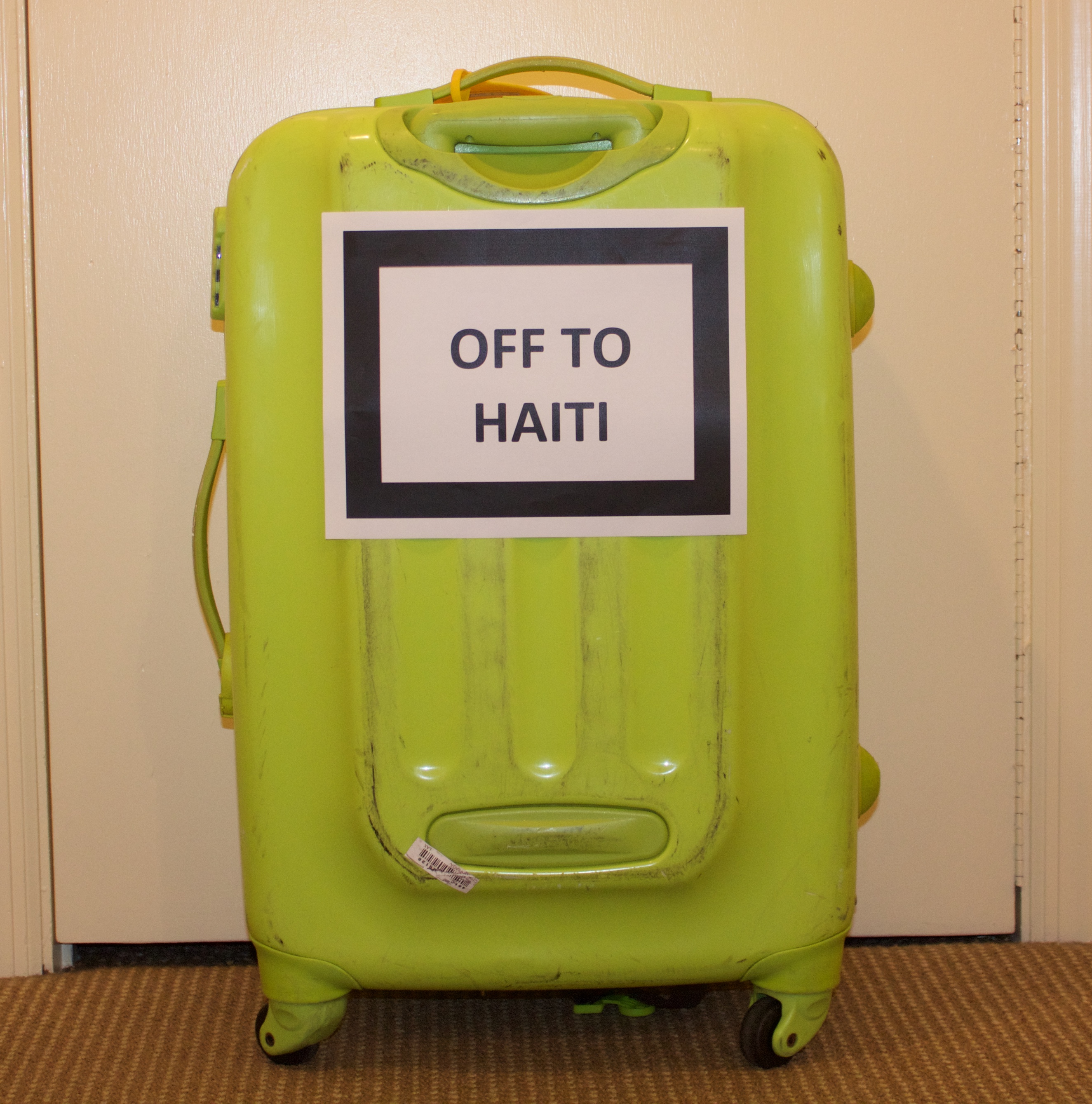 Green suitcase with Off to Haiti sign