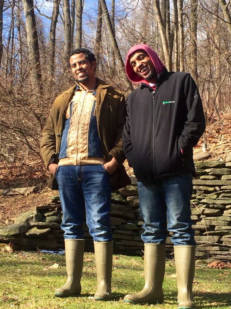 Two young Ethiopian men dressed in western clothing, including rubber boots in suburban backyard